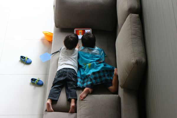 ילדים שוכבים על ספה וצופים במסך של מכשיר נייד